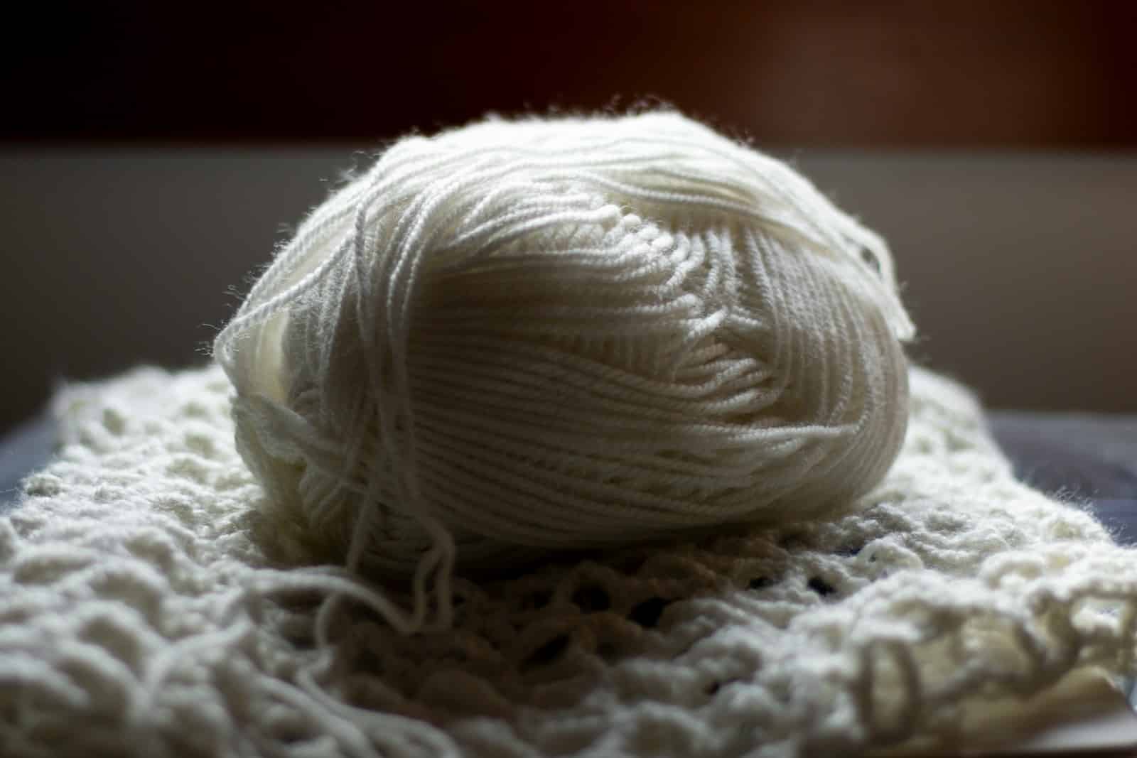 A ball of white yarn rests on knit fabric.